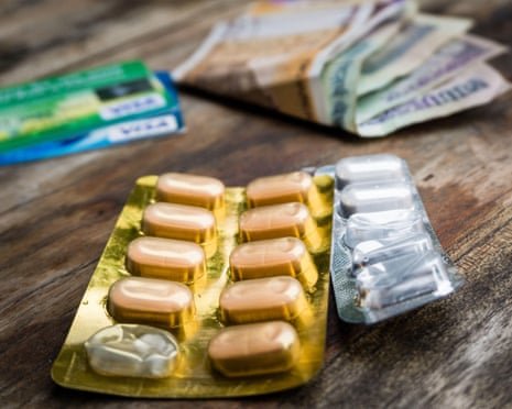Pill blister packs sit on a wooden table beside banknotes and credit cards