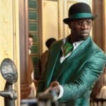 Lupin in a shimmering green suit, bowler hat, and glasses extends his hand forward