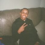 A young man sitting on a leather sofa smiles and makes a peace sign