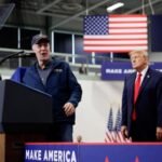 a man speaks into a microphone as Donald Trump stands behind him