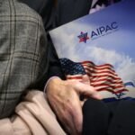 A visitor's hand holds an AIPAC folder showing American and Israeli flags